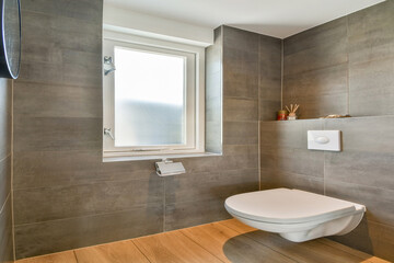 A sleek and contemporary bathroom featuring gray tiles, a window, and a stylish toilet design, capturing a minimalist aesthetic.