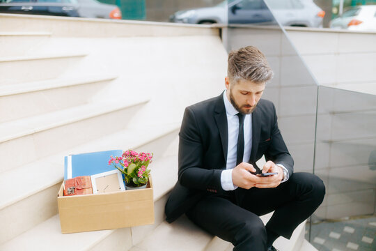 Laid-off businessman sitting on stairs checking phone for job updates