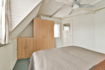 The image showcases a stylish bedroom with a neatly made bed, wooden wardrobe, and ceiling fan, creating a serene and inviting atmosphere.