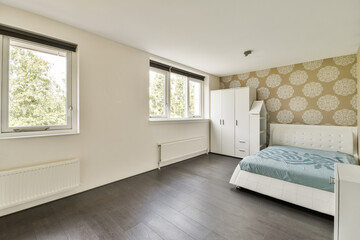 A clean and spacious modern bedroom featuring large windows, light walls, a comfortable bed, and...