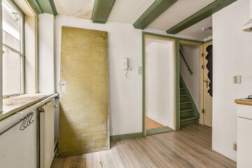 An interior shot showcasing a minimalist kitchen with wooden floors, green beams, and a door leading to an adjacent hallway. The lighting highlights the simplicity of the space.