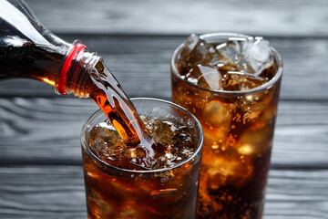 Pouring refreshing cola from bottle into glass at grey wooden table, closeup