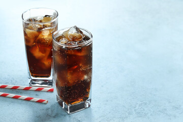 Refreshing cola with ice cubes in glasses and straws on light textured table, closeup. Space for text