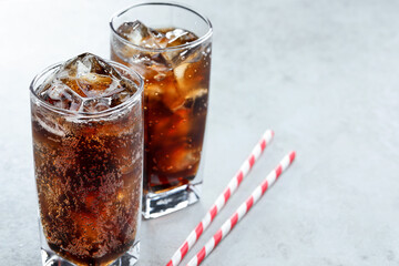 Refreshing cola with ice cubes in glasses and straws on light table, closeup. Space for text