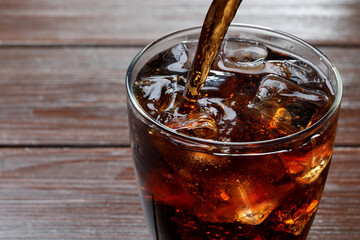 Pouring refreshing cola into glass at wooden table, closeup. Space for text