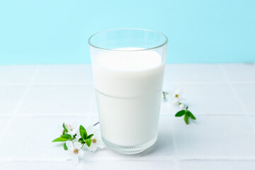 Glass of fresh milk and blossoms on white tiled table against light blue background