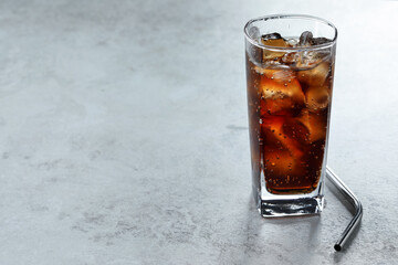 Refreshing cola with ice cubes in glass and straw on grey textured table, closeup. Space for text