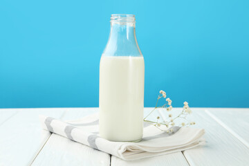Fresh milk in glass bottle and flowers on white wooden table against light blue background