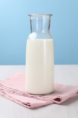 Fresh milk in jug on white wooden table against light blue background