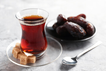 Traditional Turkish tea in glass cup, brown sugar and dates on light grey table, closeup