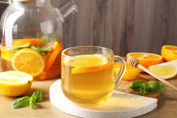Aromatic fruit tea in glass cup, teapot, orange, lemon, honey and mint on wooden table, closeup