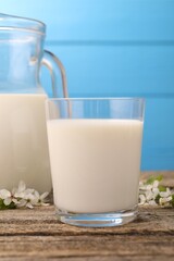 Fresh milk and blossoms on wooden table against light blue background, closeup