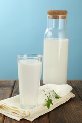 Fresh milk and blossoms on wooden table against light blue background