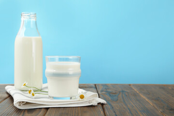 Fresh milk and flowers on wooden table against light blue background, closeup. Space for text