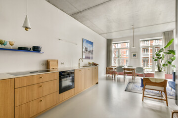 Stylish interior featuring a contemporary kitchen with wooden cabinets, a dining area, and natural light flooding through large windows, creating a welcoming atmosphere.