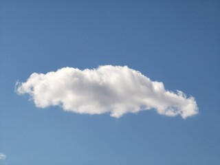 Large, puffy white cloud with an elongated shape floats against a clear blue sky, creating a clean,...