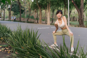 Asian woman stretching before workout outdoors in park, wearing athletic attire, surrounded by...