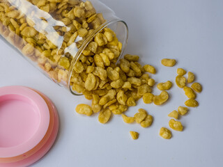 Crunchy broad beans spilling from a glass jar on a white surface
