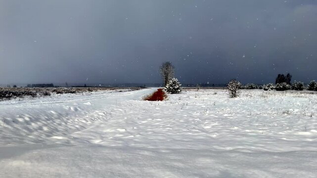 Bleak winter road under ominous storm clouds, fresh snow falling in Pinki village. Striking red patch mars the white expanse. Low-angle, wide shot captures desolate, cold landscape, descend