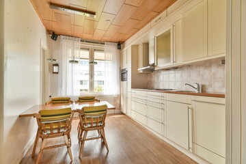 A sleek modern kitchen featuring light wood accents and a dining table with wooden chairs near a window, highlighting a bright and inviting space.