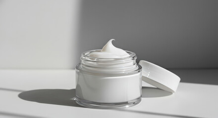Creamy moisturizer in a clear jar on a simple background