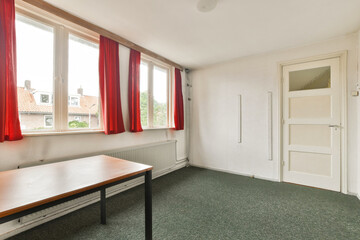 A bright, unfurnished room featuring large windows draped with red curtains. The space has a minimalistic design and neutral-colored walls, ideal for various uses.