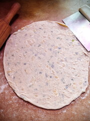 rolled khychiny with onion, cheese, and potato filling, resting next to a dough scraper on a prep surface