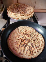 flat khychiny with onion, cheese, and potato filling cooking in a pan, golden and sizzling on the stove
