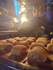 unbaked sourdough cinnamon rolls baking on a baking sheet in the oven with a swirl of cinnamon filling in oven light