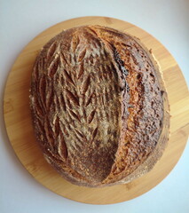 freshly baked artisanal whole wheat sourdough bread with rustic crust cooling on a round metal rack surface side view