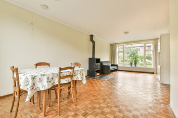 A spacious living area featuring a dining table, chairs, and a small seating arrangement by a window, complemented by natural light and minimal decor.