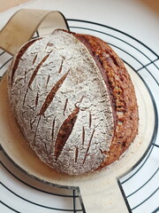 freshly baked artisanal whole wheat sourdough bread with rustic crust cooling on a round metal rack and silicone pad
