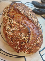 freshly baked artisanal whole wheat sourdough bread with rustic crust with seeds cooling on a round metal rack and silicone pad surface