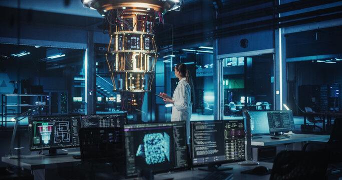 Female Computer Scientist Developing Quantum Machine Learning Algorithms, Using a Tablet Computer to Simulate and Test Their Performance. She is Standing in an Advanced Dark Office Alone