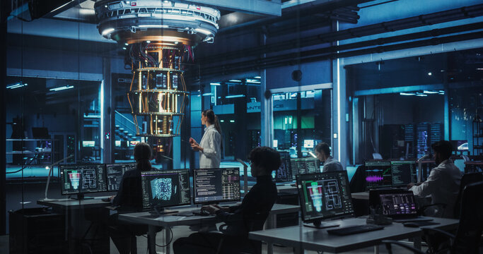 Female Engineer Working on Quantum Computer Hardware, Using Tablet Computer to Access Technical Specifications and Control Processor Parameters. Group of Developers Work on AI Behind a Desk