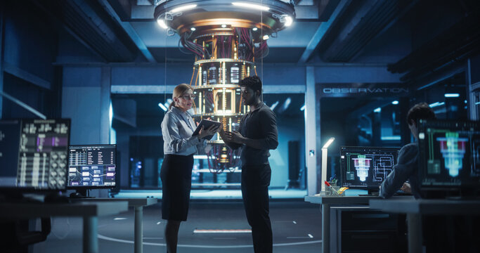 Middle Aged Caucasian Female Team Leader and Young Indian Scientist Talking in a Research Center with a Futuristic Quantum Computer Device. Specialists Discussing Machine Learning Development