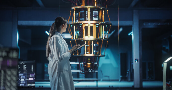 Female Computer Engineer Examining a Quantum Computer in a High Tech Scientific Laboratory. Professional Scientist in White Coat Typing Research and Development Analytics in Her Tablet Computer