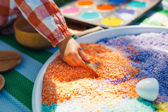Child plays with colorful rice in sensory activity at outdoor learning space