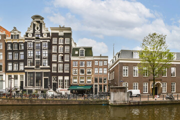 Historic buildings line the serene canals of Amsterdam, showcasing architectural beauty against a vibrant sky. A picturesque setting for urban exploration.