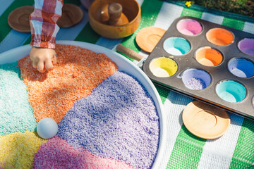 Colorful sensory play station with rice and paint on grass in sunny park