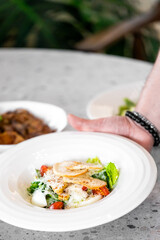A close-up of a fresh salad topped with crispy croutons, cherry tomatoes, and greens is presented on a marble table, highlighting a delicious and healthy dining option.