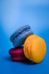 Stack of three colorful macarons—blue, yellow, and magenta—arranged artistically against a vibrant blue background, highlighting their texture and cheerful tones