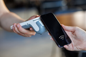 Customer paying via smartphone using NFC contactless payment technology at retail checkout.