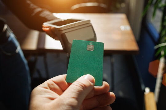 Green card ready for wireless payment at terminal in modern cafe with natural lighting.