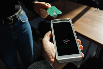 Customer making contactless payment with credit card and terminal in natural light.