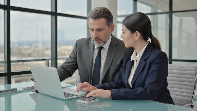 Mature Latin business man mentoring mid age European business woman discussing project on laptop in office Two colleagues, group of partners, businessman and businesswoman working