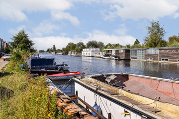 A serene scene featuring a calm waterway lined with houseboats and greenery on one side, capturing...