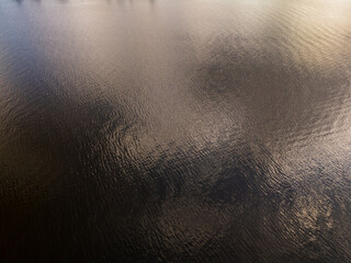 Calm water creates ripples under a gray sky, reflecting soft hues of light. The peaceful ambience...