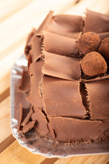 Chocolate cake, close-up of a chocolate cake decorated with curled chocolate shavings and dusted cocoa truffles on a silver tray over a rustic wooden surface, selective focus.
