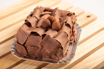 Chocolate cake, close-up of a chocolate cake decorated with curled chocolate shavings and dusted cocoa truffles on a silver tray over a rustic wooden surface, selective focus.